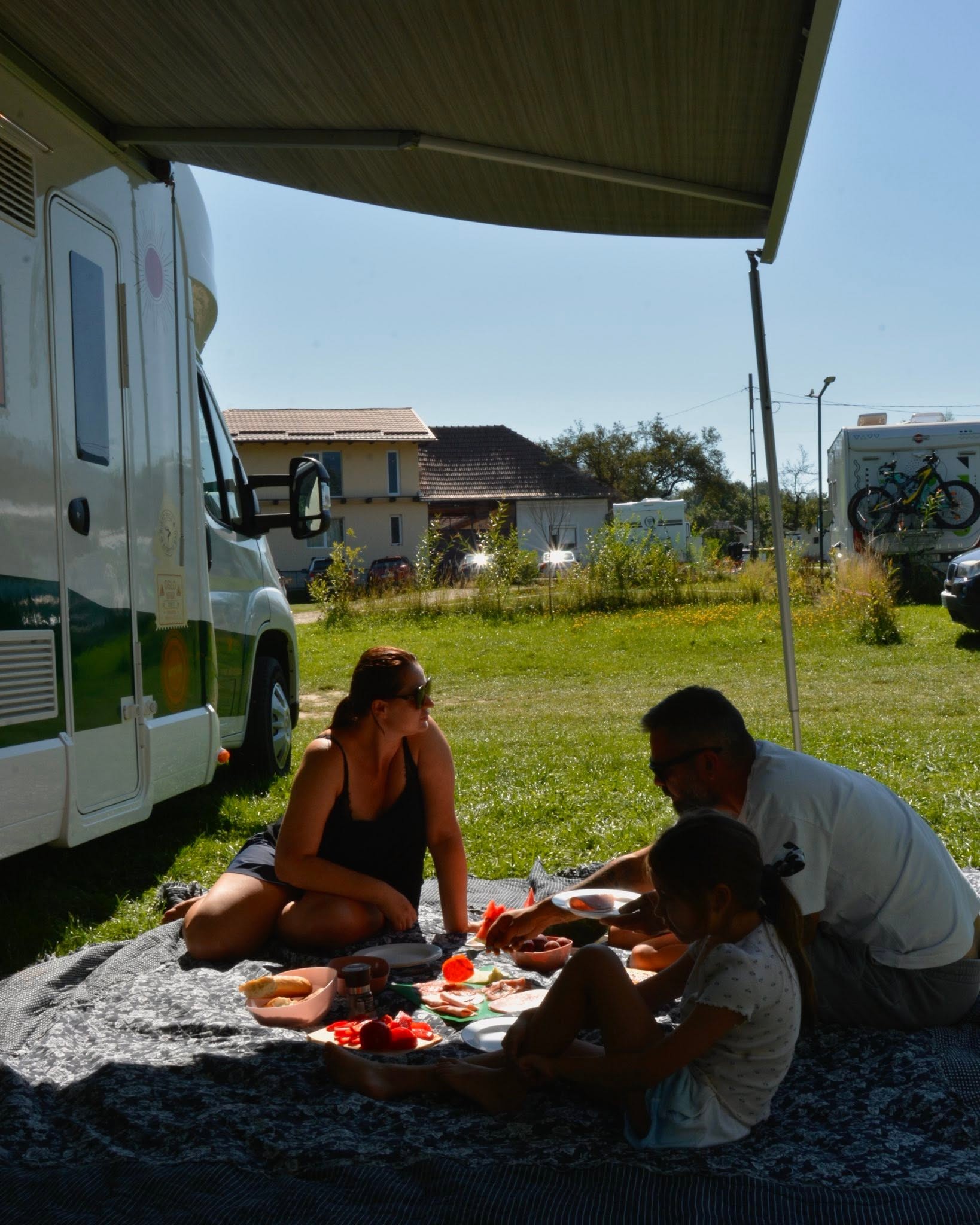 Familie luând masa la umbra unei rulote CampVentures, într-o zi de vară